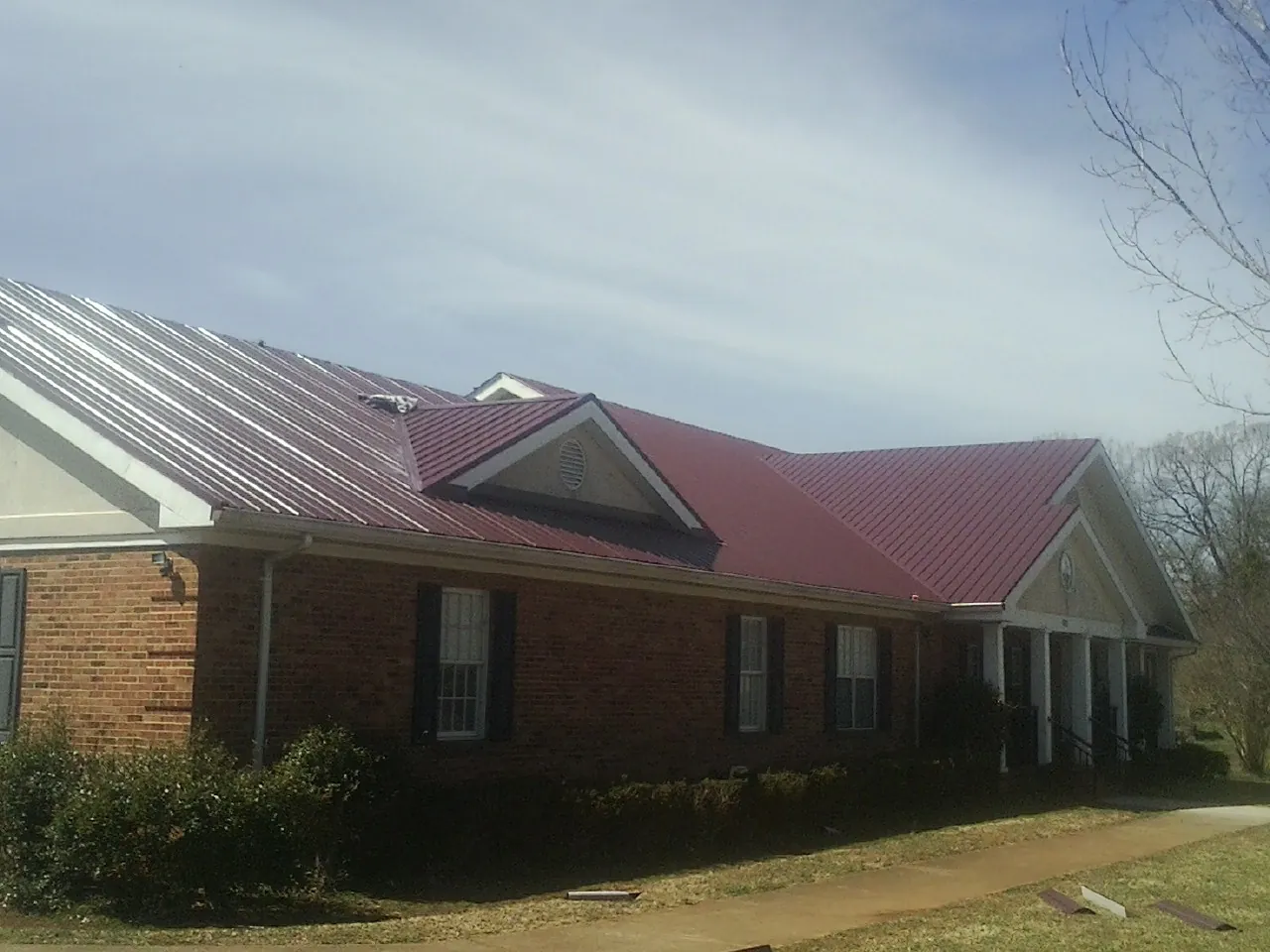 Red metal roof with gabled entries on a long brick building, from a Hail Damage Roof Repair job in Mc Knightstown