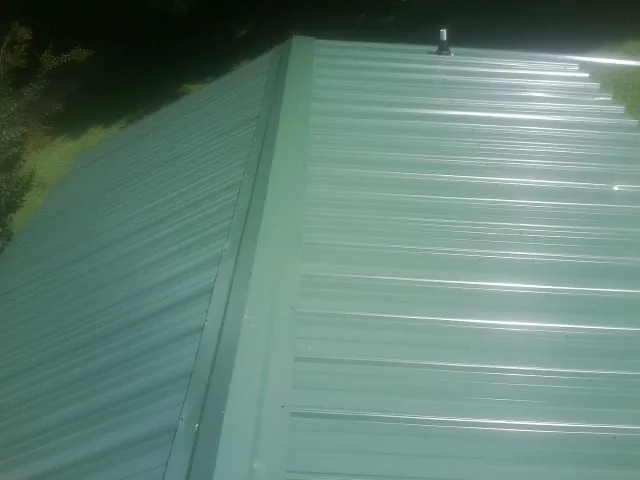 New green metal panels meeting at the ridge of a roof — Flat Roof Repair work by our crew in Mc Knightstown