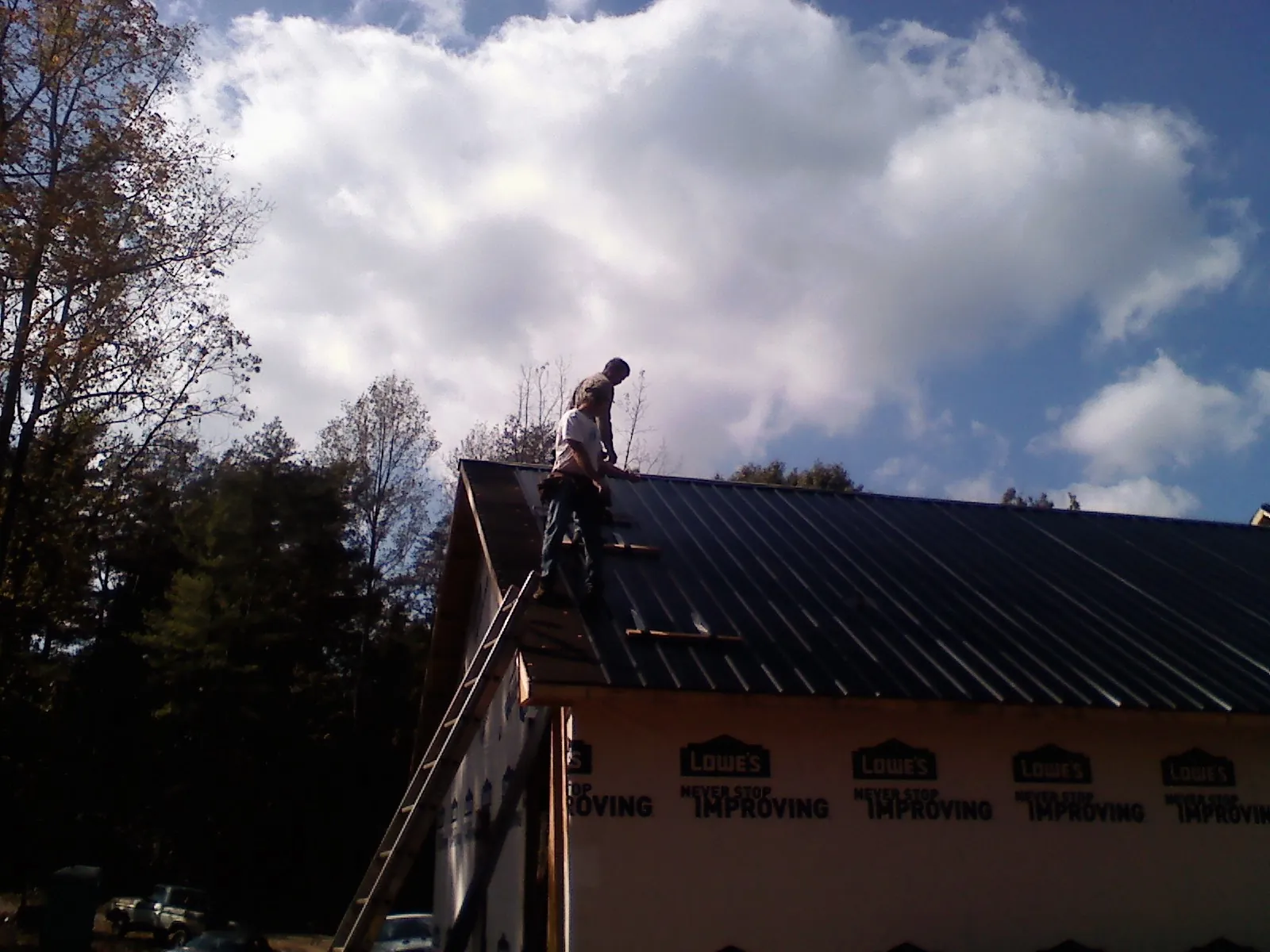 Roofer fastening dark metal panels high against a cloudy sky, from a Roof Inspection job in Mc Knightstown