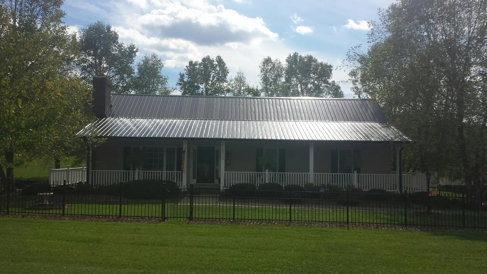 Gray metal roof on a brick ranch with a full width front porch — Gutter Guard Installation work by our crew in Mc Knightstown