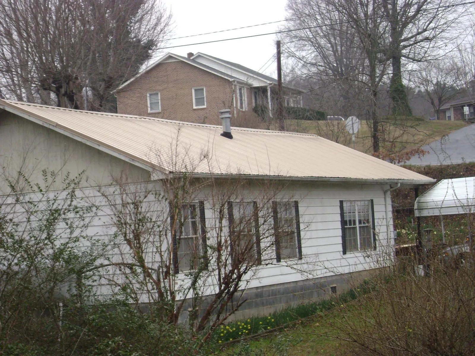 Tan metal roof on a white sided house set into a hillside — Commercial Roofing by Roofing Brothers in Mc Knightstown